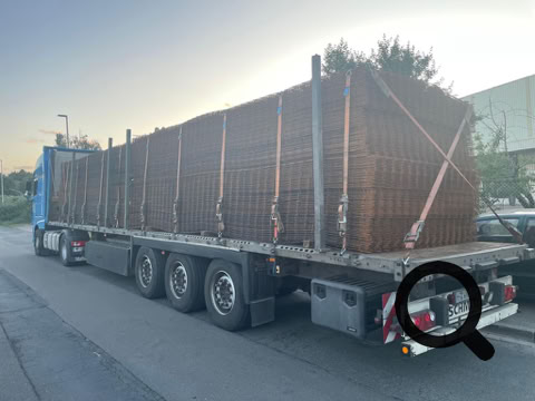 LKW mit Anhänger, beladen mit gestapelten Metallgittern, auf einer Straße geparkt.